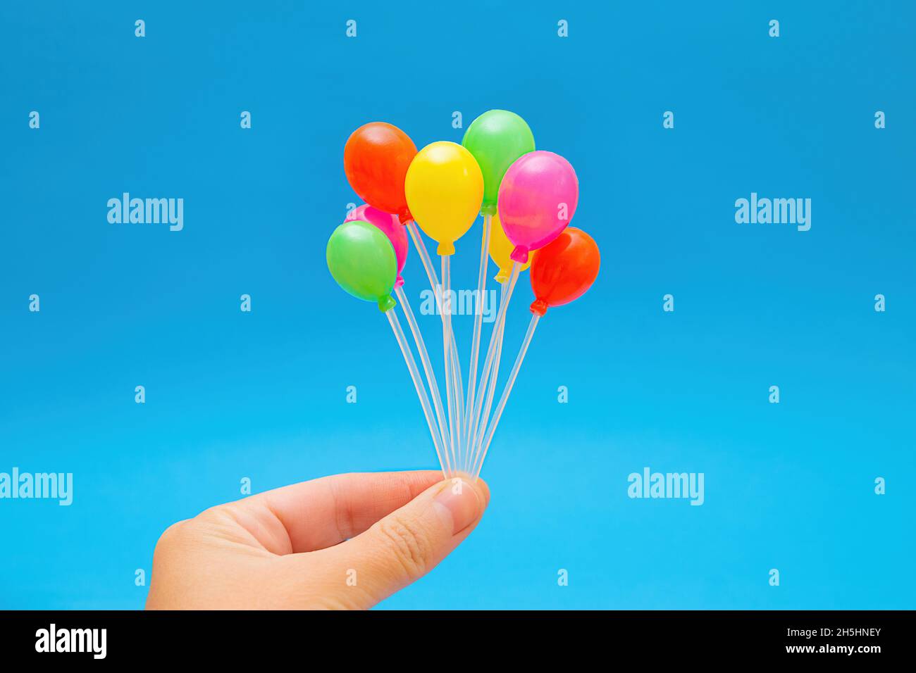 Cluster von bunten winzigen Plastikballons in der Hand vor einem blauen Hintergrund Stockfoto