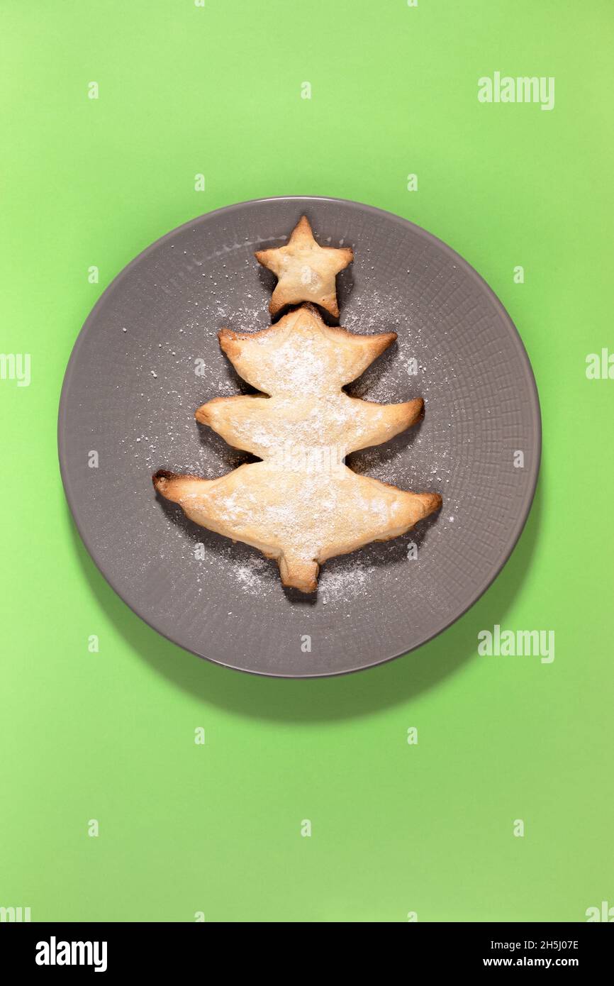 Hausgemachte kreative gebackene Plätzchen als Weihnachtsbaum auf runden grauen Teller auf grünem Hintergrund. Urlaub Backen für Kinder Idee. Weihnachten festliche Speisen minimal imag Stockfoto