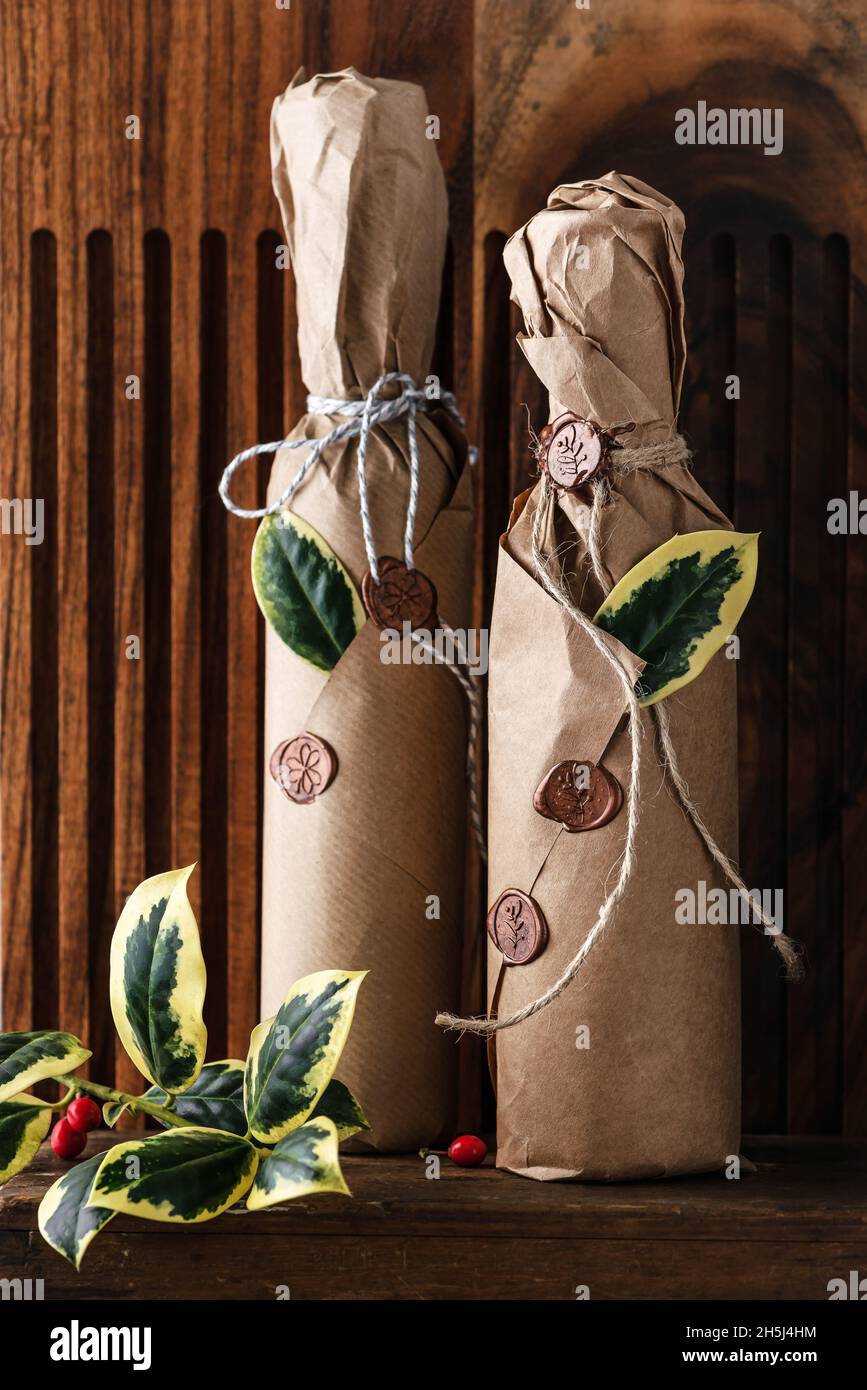 Hausgemachter Obstwein in den Flaschen, dekoriert mit Grunge-Papier, Wachssiegel und grünen Stechpalmblättern als kleines Geschenk zu Weihnachten. Geschenkideen für die Küche Stockfoto