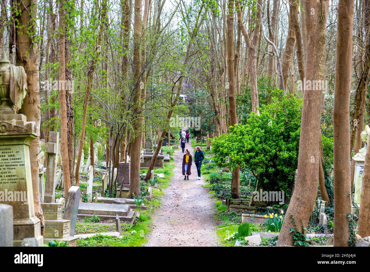 Menschen, die auf einem von Gräbern gesäumten Pfad auf dem Highgate Cemetery East, London, Großbritannien, gehen Stockfoto