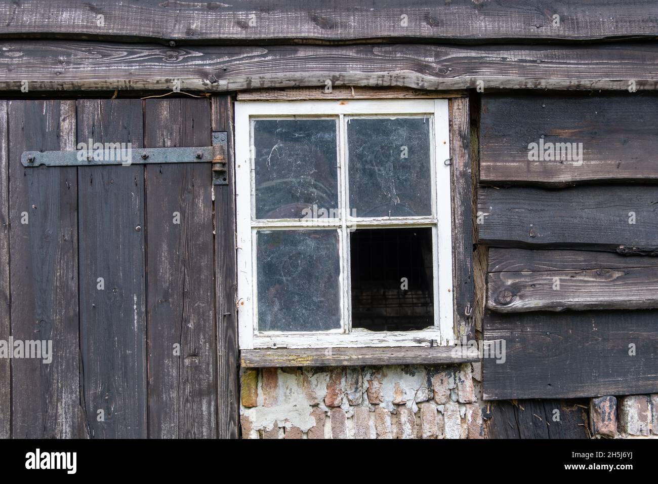 Blick auf verwitterte Türen, Fenster und Stallbretter verfallener und verlassener Stallungen auf einem Bauernhof auf dem Land in den Niederlanden Stockfoto