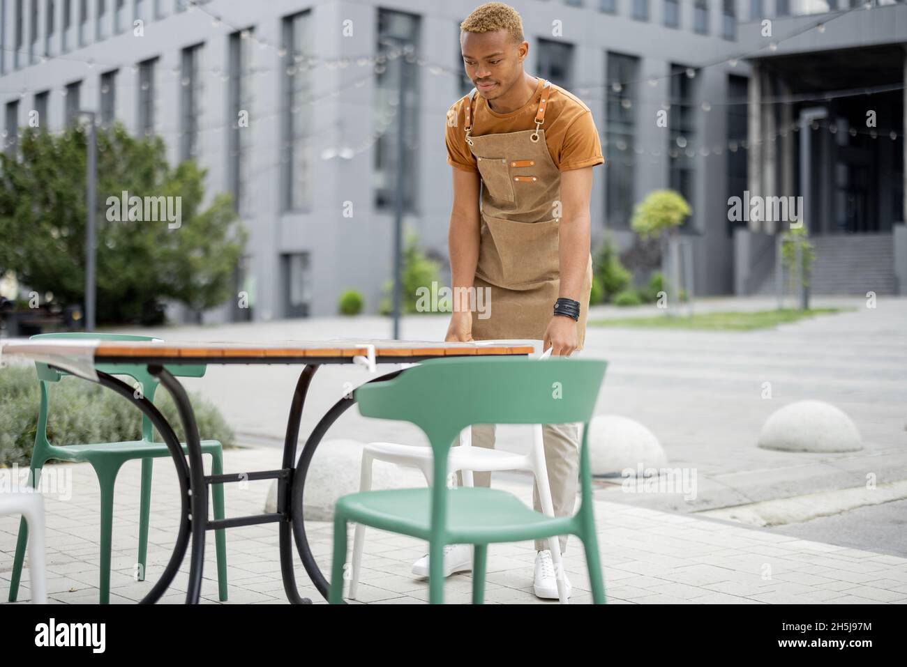 Der Kellner korrigierte den Stuhl am Tisch im Café im Freien Stockfoto