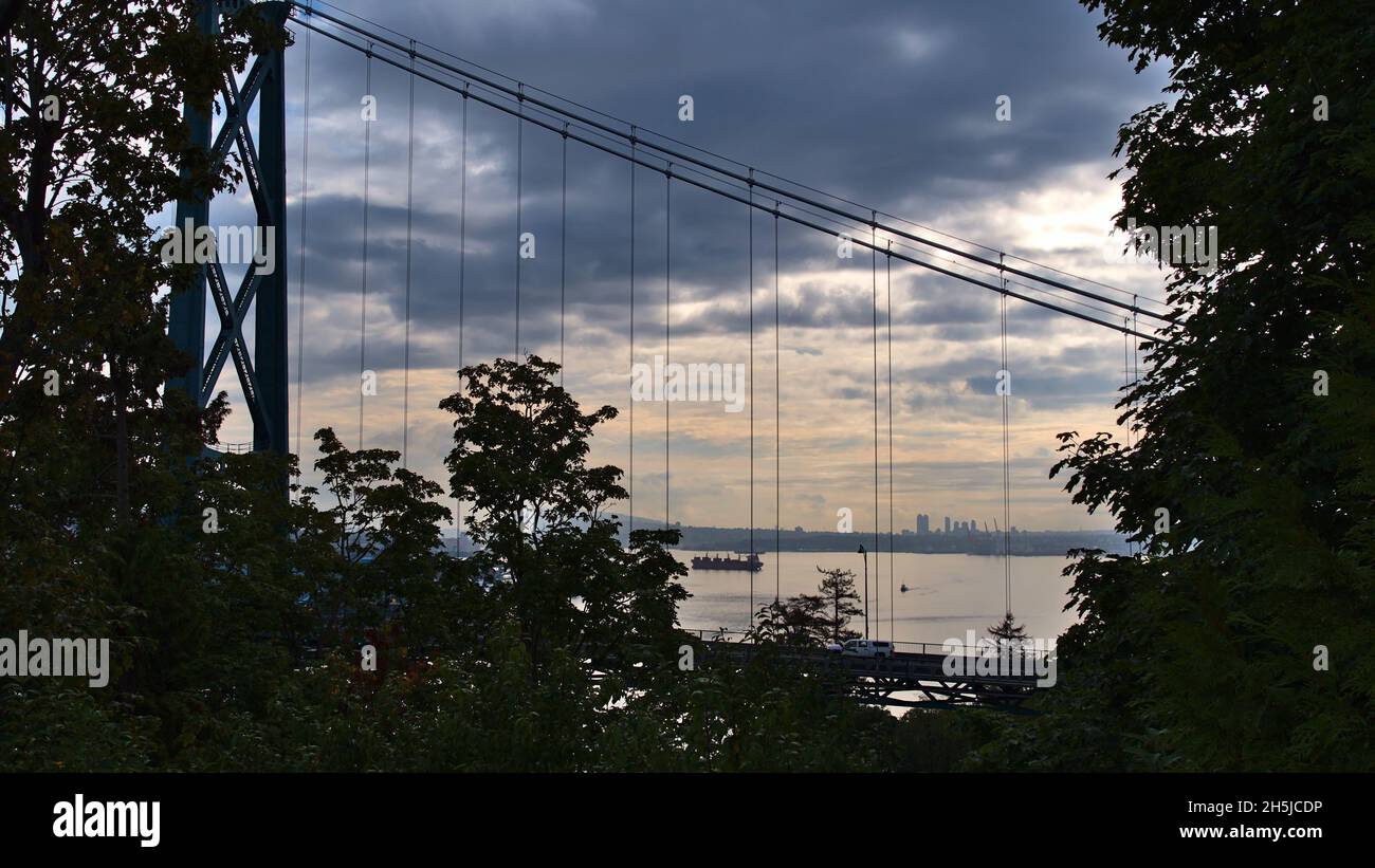 Blick auf den Burrard Inlet am Morgen mit Silhouetten von Laubbäumen vor der Tür und die Lions Gate Bridge vom Stanley Park, Vancouver, Kanada. Stockfoto