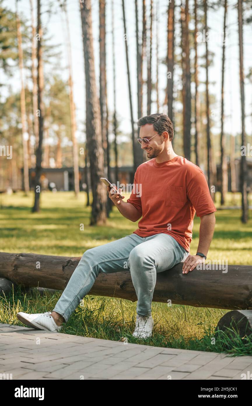 Lächelnder Mann mit Smartphone sitzt in der Natur Stockfoto