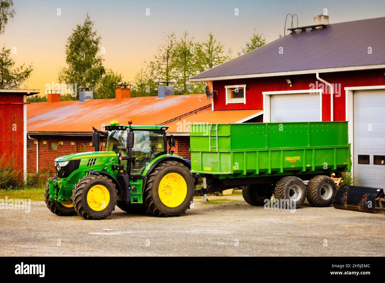John Deere 6155R Traktor vor dem Palmse 1900 Anhänger auf dem Hof im Morgenlicht. Salo, Finnland. 29. August 2020. Stockfoto