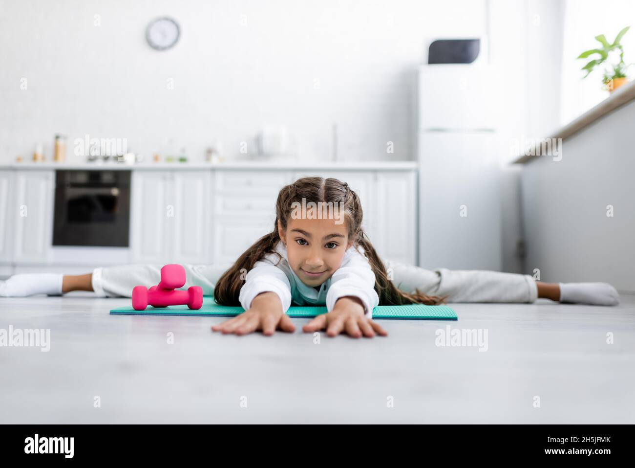 Oberflächenhöhe des Kindes, das die Kamera anschaut, während es in der Nähe von Kurzhanteln in der Küche gespalten wird Stockfoto