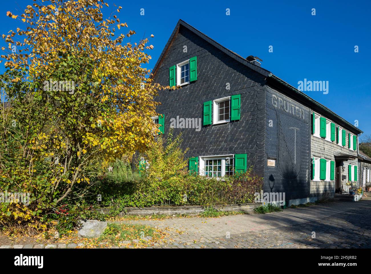 Deutschland, Haan, Bergisches Land, Niederbergisches Land, Niederberg, Rheinland, Nordrhein-Westfalen, NRW, Haan-Gruiten, historisches Dorf Gruiten, Kircherhof, ehemaliger Hofhof, Fachwerkhaus mit Schieferfassade und grünen Fensterläden, Herbstfärbung Stockfoto