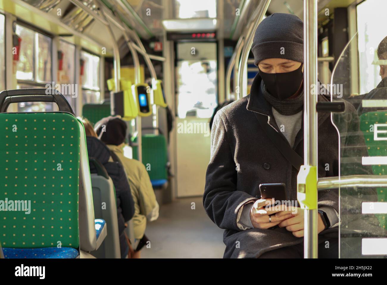 Junger Mann in einer Gesichtsmaske mit einem Smartphone für soziale Medien im öffentlichen Verkehr Stockfoto