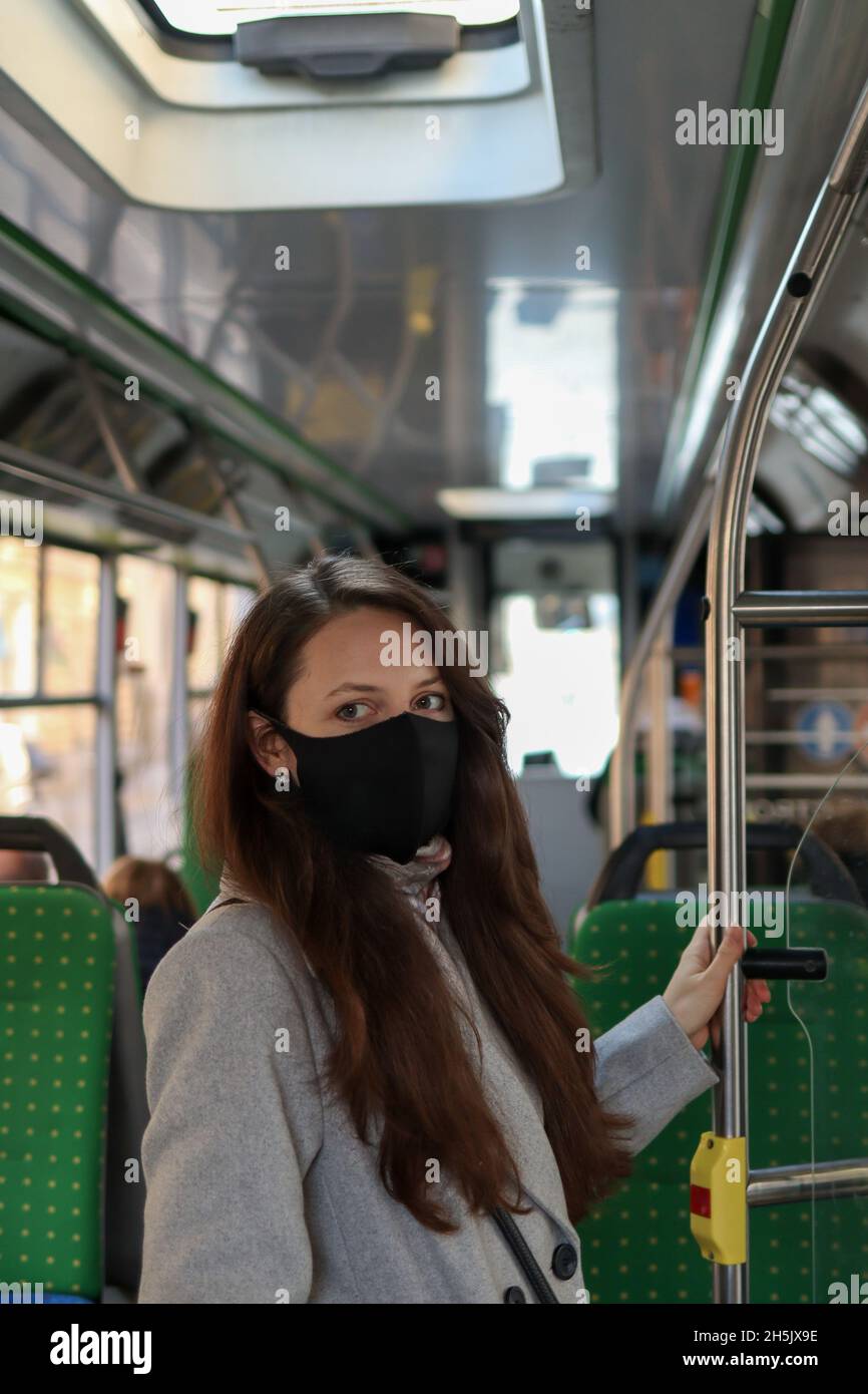 Junge europäische Passagierin mit Gesichtsmaske und Blick auf die Kamera im Bus Stockfoto