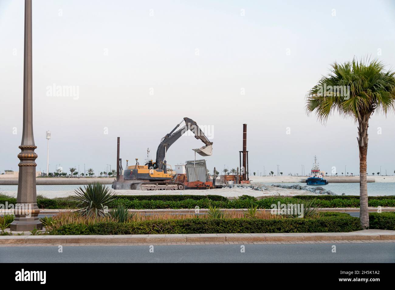 An der Küste des Persischen Golfs in Abu Dhabi, VAE, wird ein Bagger auf einem Kahn von einem Caisson abgehoben. Stockfoto