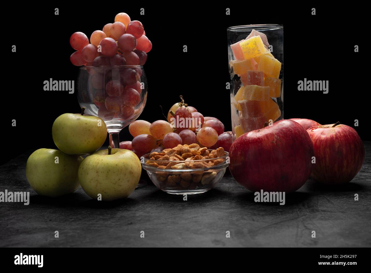 Verschiedene, sortierte Früchte (Trauben-, Apfel-, Nüsse- und Ananasstückchen), auf einer schwarzen Marmorplatte, schwarzer Hintergrund mit weichem Schatten Stockfoto