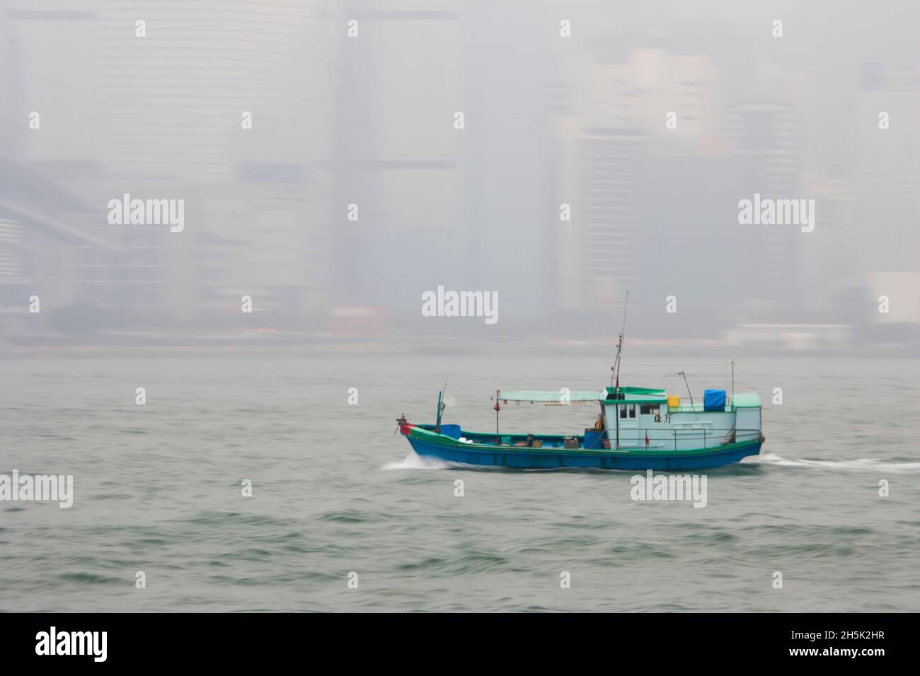 Ein Boot überquert den Hafen vor einer nebligen Hong Kong. Stockfoto