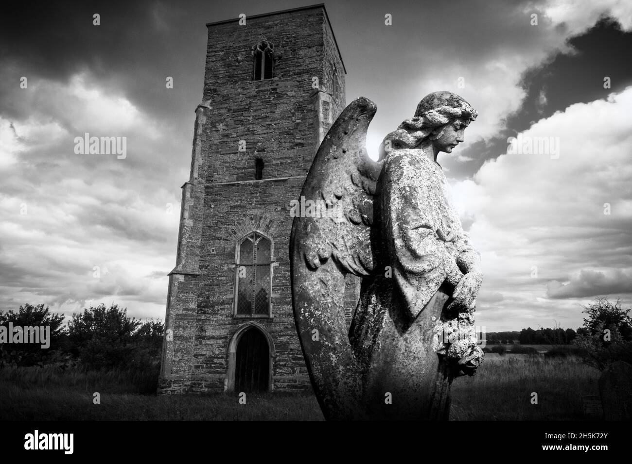 Bild einer geschnitzten Engelsfigur Grabstein vor einer Kirche auf einem Friedhof mit dramatischem schwarz-weißen Himmel. Stockfoto