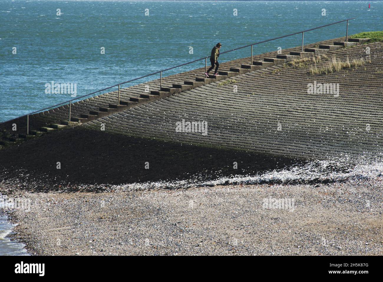 Frau geht auf einem Deich am Meer in Colijnsplaat, Oosterschelde, Zeeland, Niederlande, eine lange Treppe hinauf Stockfoto