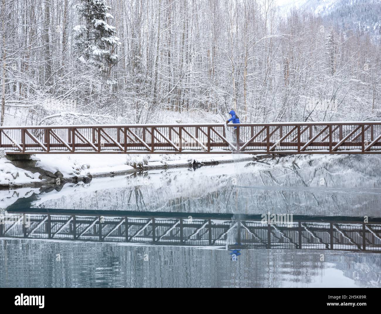 Junge, der mit dem Schnee spielt und im Winter über eine Fußgängerbrücke am Knik River entlang des Old Glenn Highway läuft; Palmer, Alaska, USA Stockfoto