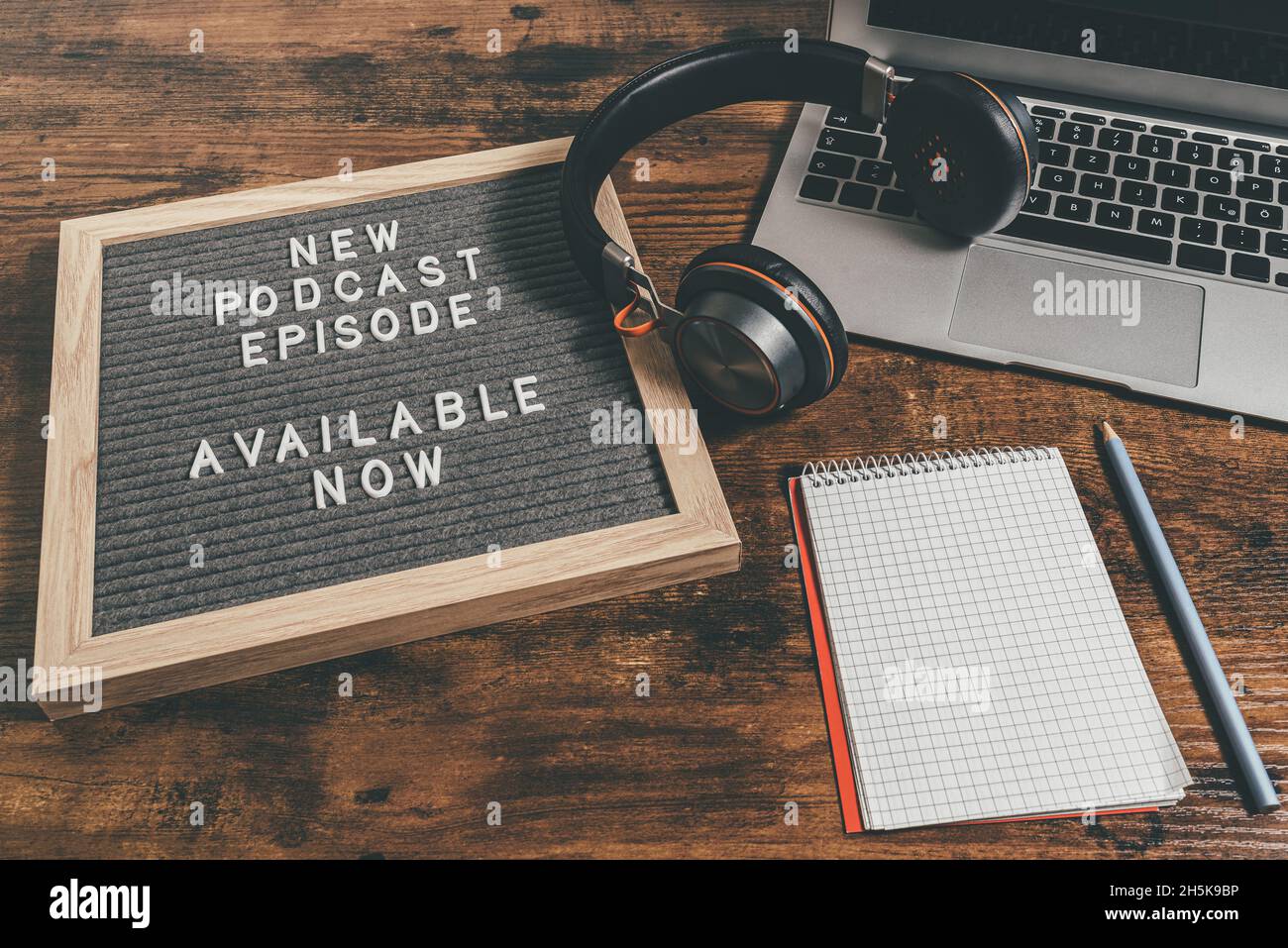 Briefbrett mit Text NEUE PODCAST-EPISODE auf Holztisch mit Laptop, Notizblock und Kopfhörer, Podcasting-Konzept Stockfoto