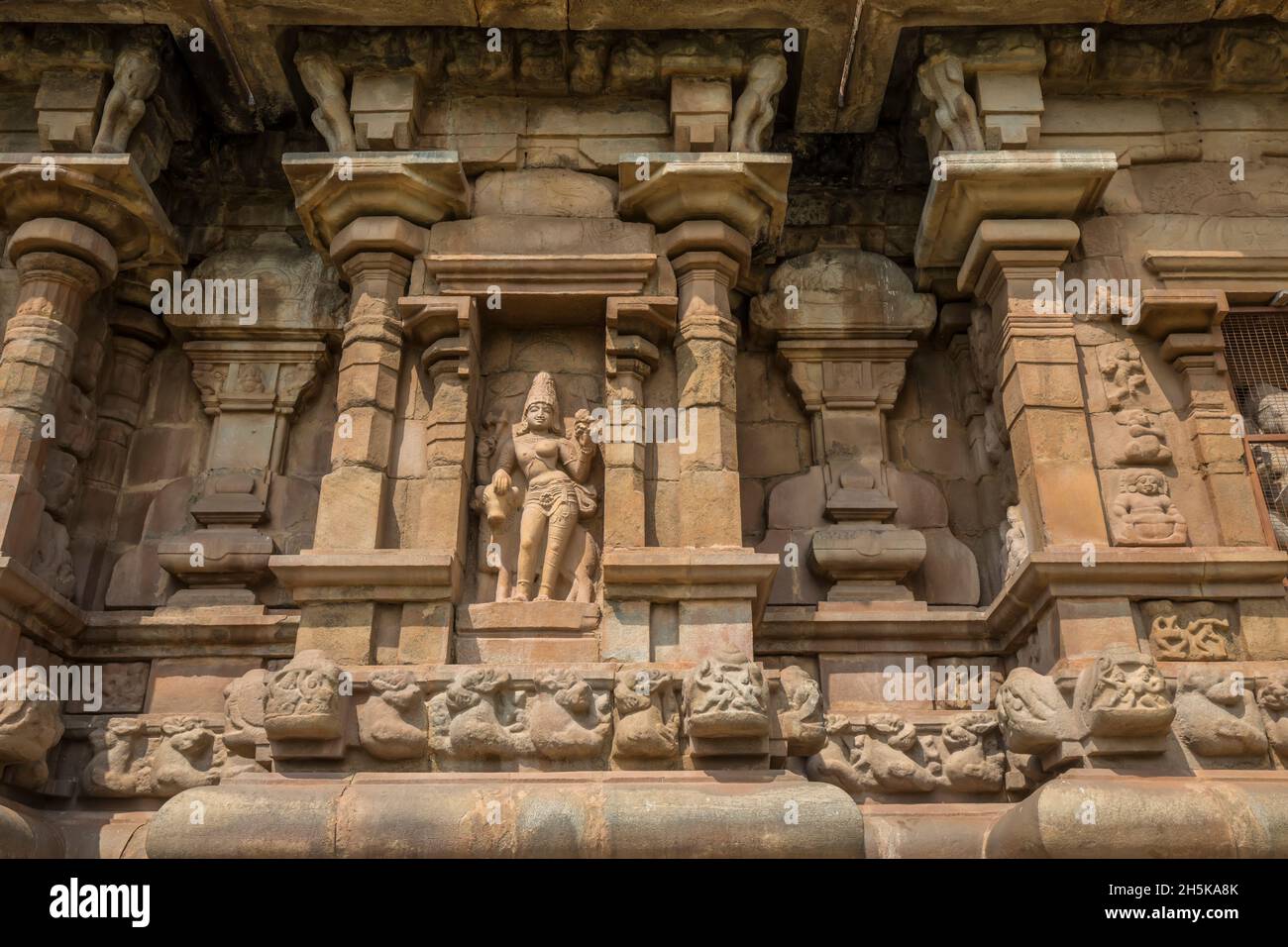 Nische mit hinduistischer Gottheitsschnitzerei in Steinmauer des Dravidischen Chola-Tempels der Airavatesvara-Ära mit Säulen und Reliefskulpturen Stockfoto
