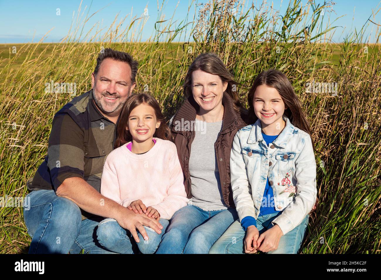 Familie mit zwei jungen Mädchen sitzen auf ihrem Ackerland, Alcomdale, Alberta, Kanada, für ein Porträt Stockfoto