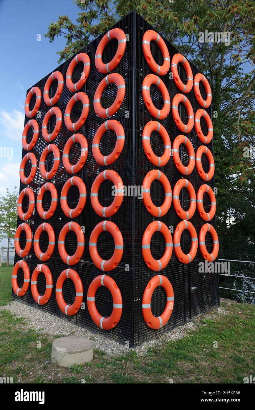 Schwarzer Gitterwürfel mit leuchtend orangefarbenen Rettungsbojen am Rheinufer, Huningue, Haut Rhin, Elsass, Grand Est, Frankreich Stockfoto