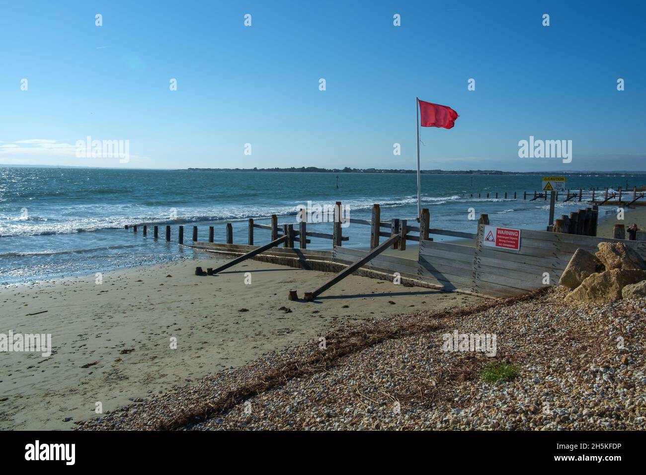 Sonne, Meer und Himmel, in East Head, West Wittering, Chichester Harbour, VEREINIGTES KÖNIGREICH. Defensive Groynes verlängern die Meeresrauschen. Die rote Flagge fliegt, um vor Gefahr zu warnen. Stockfoto