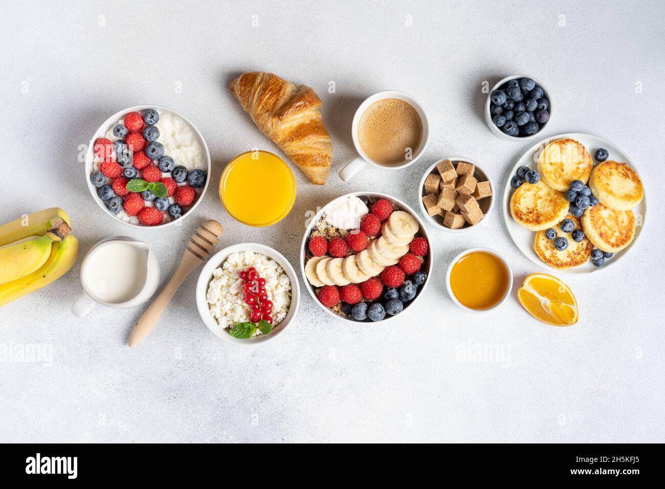 Morgens serviertes Frühstücksset: Pfannkuchen, Haferbrei, Hüttenkäse, Müsli, Müsli, Orangensaft, Tee, Kaffee, Obst und Beeren. Stockfoto