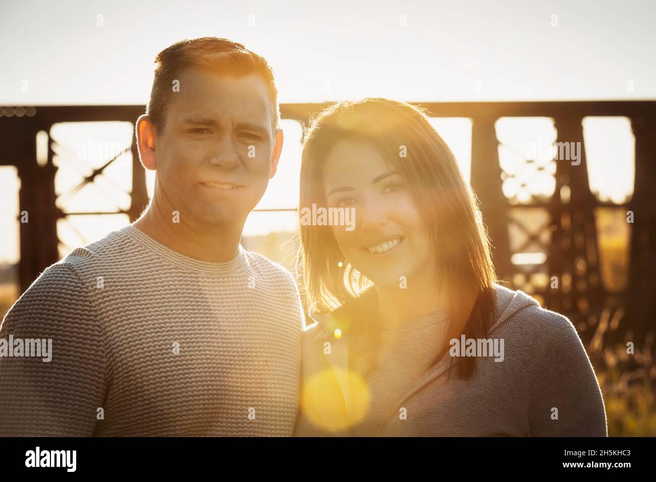 Porträt eines Ehepaares mittlerer Erwachsenen im Herbst bei Sonnenuntergang in einem Park mit einer Brücke hinter ihnen; St. Albert, Alberta, Kanada Stockfoto