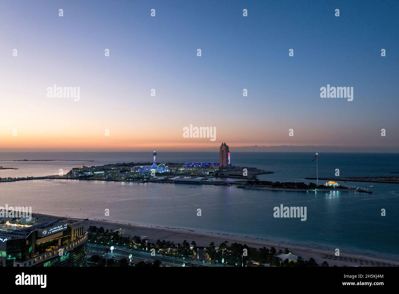 Die Sonne untergeht hinter Marina Island am Persischen Golf in Abu Dhabi, VAE. Ein Vergnügungspark scheint gegen die Dämmerung, als das ungeöffnete Atlantis Hotel si... Stockfoto