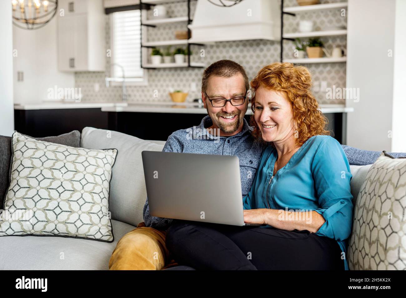 Verheiratetes Paar, das zu Hause mit seinem Laptop auf einer Couch sitzt; Edmonton, Alberta, Kanada Stockfoto