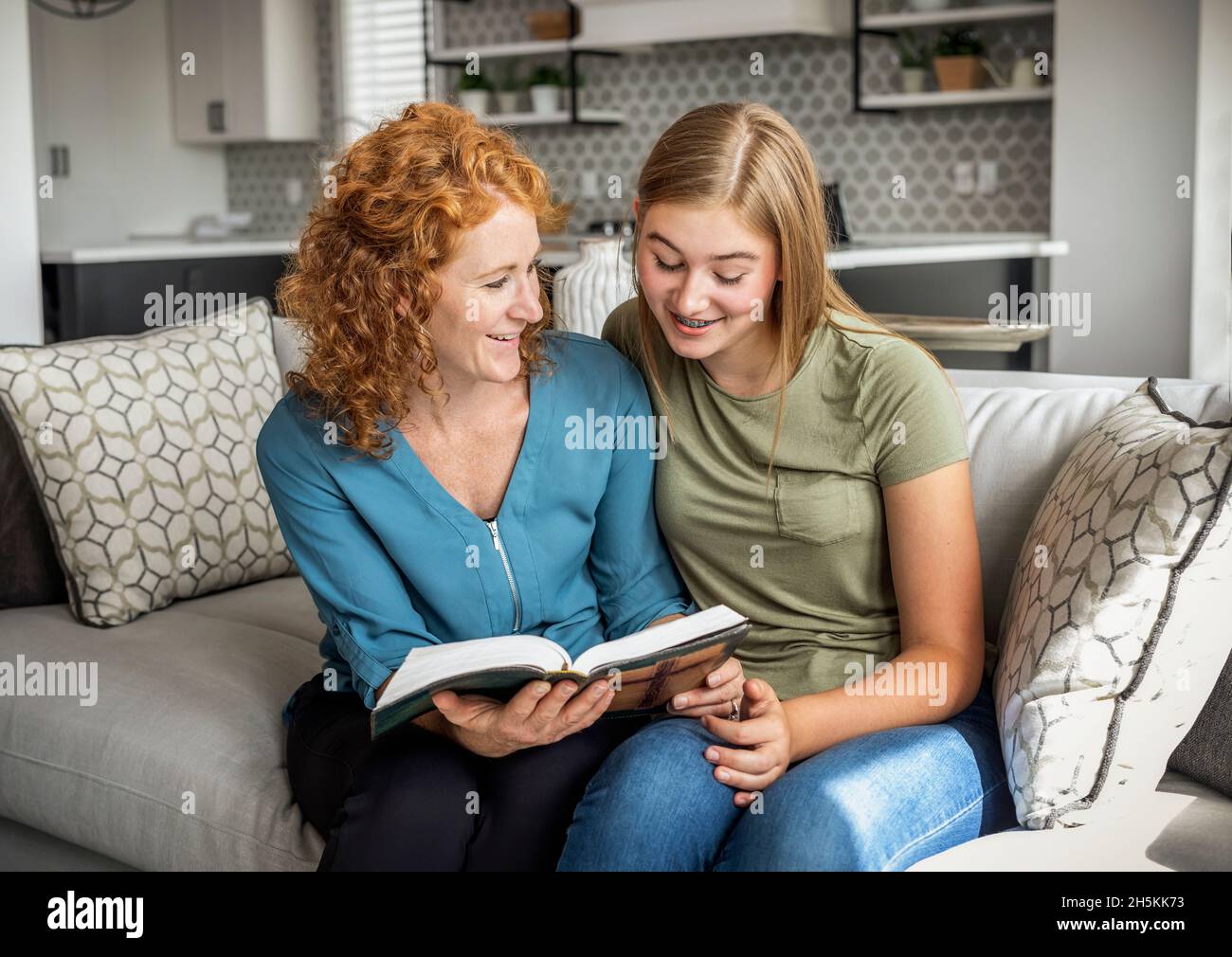 Mutter und Tochter im Teenageralter sitzen zu Hause auf einer Couch und lesen gemeinsam die Bibel; Edmonton, Alberta, Kanada Stockfoto
