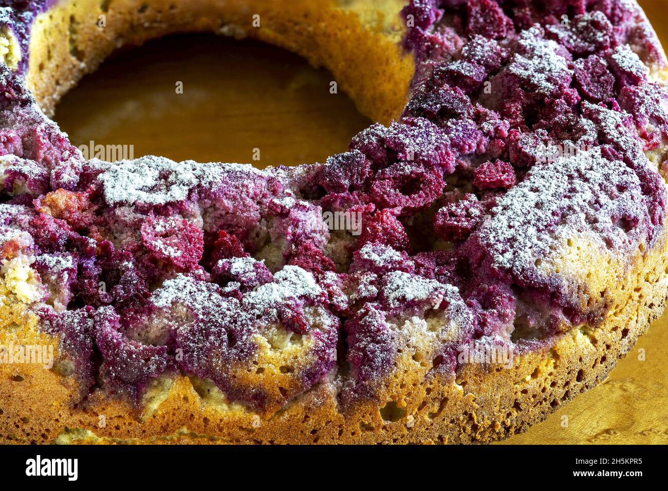 Nahaufnahme einer Himbeere, die auf einen Zuckerkuchen übertaut wird; Studio Stockfoto