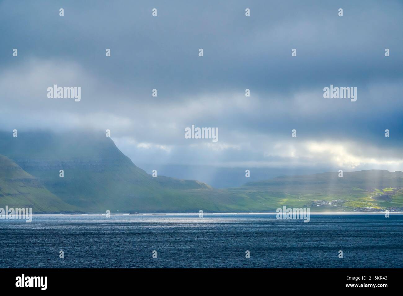 Blick von der Inselfähre Norrona auf die Färöer-Inseln, mit Sonnenlicht, das durch die Wolken zum Wasser strömt und unten landet Stockfoto