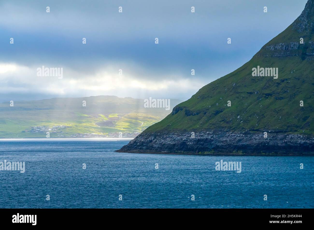 Blick von der Inselfähre Norrona auf der Fahrt durch die Färöer-Inseln, mit Sonnenlicht, das durch die Wolken zum Wasser strömt und unten landet Stockfoto