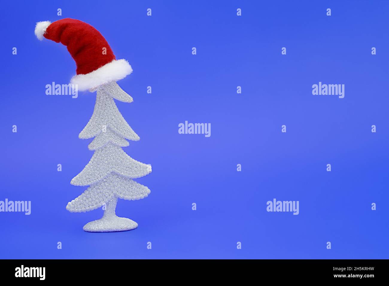 Weißer, glänzender Weihnachtsbaum mit Weihnachtsmann-Hut auf dem Kopf auf blauem Hintergrund. Neujahr. Speicherplatz kopieren Stockfoto