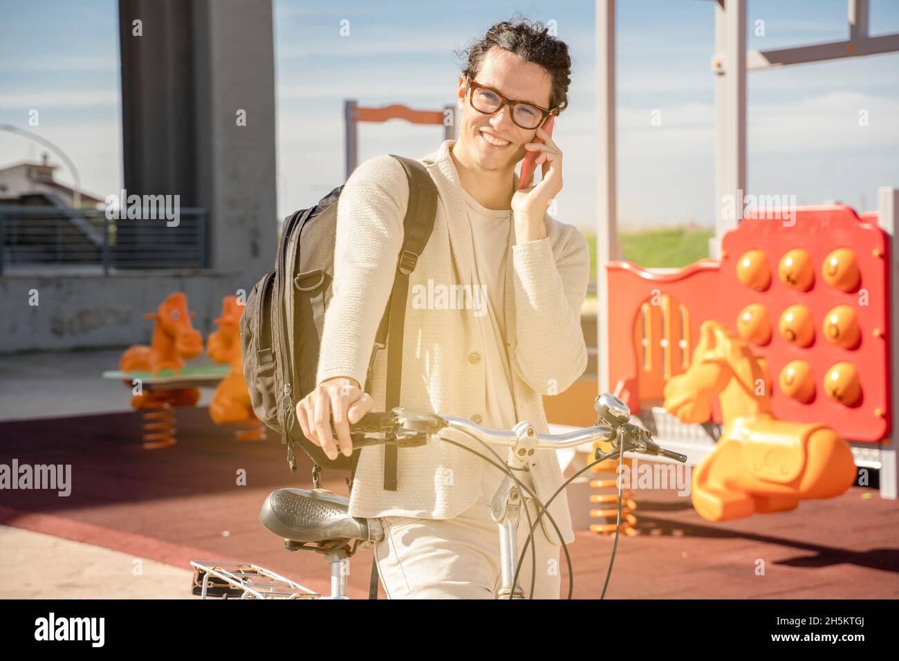 Junge fröhlich kaukasischen Hipster männlich mit Fahrrad mit Handy. Glücklich lächelnder Kerl Radfahrer mit Rucksack Stockfoto
