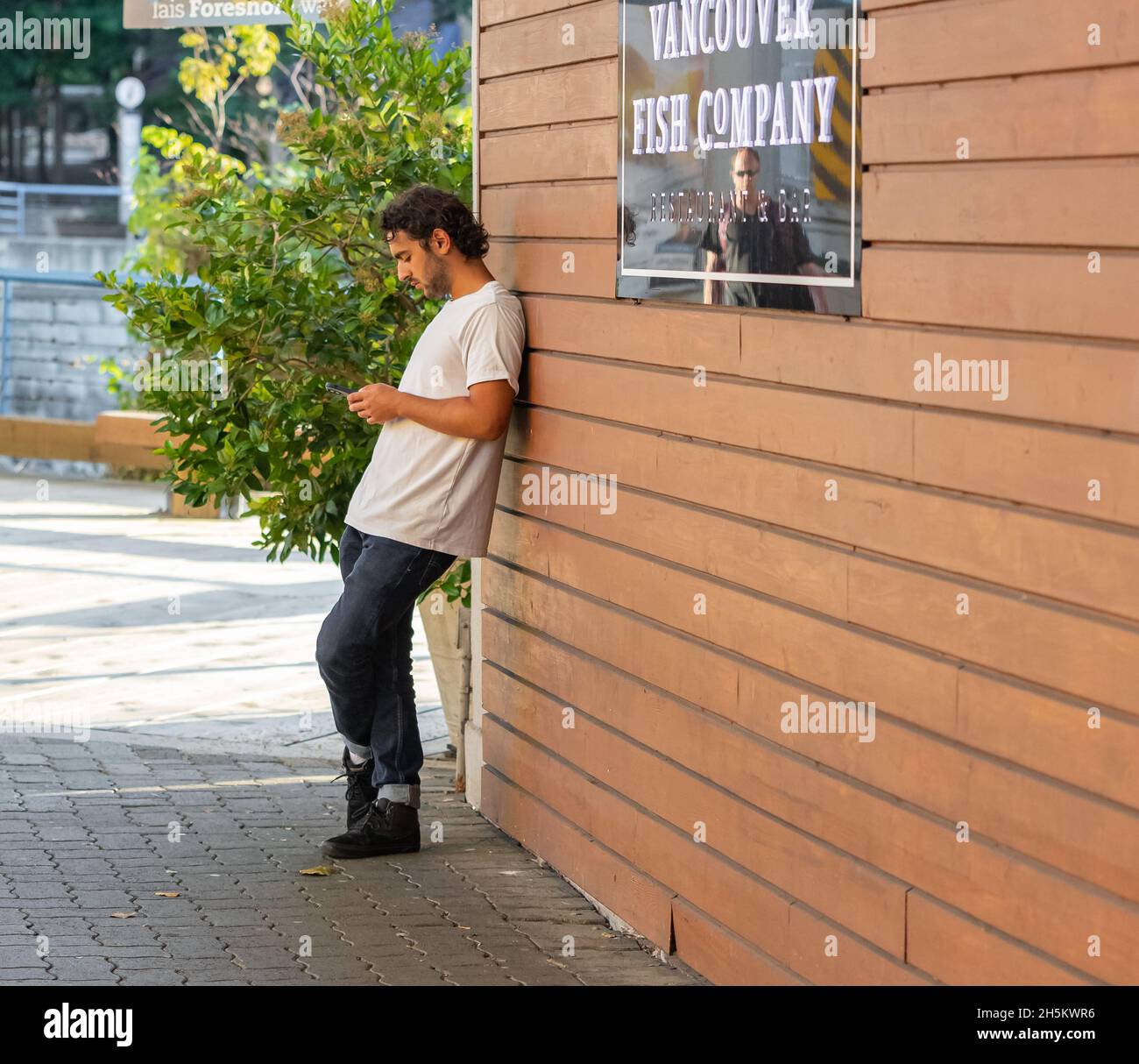 Foto eines jungen Mannes in legerer Kleidung, der sich in einer Stadt an einer Holzwand lehnt. Stockfoto