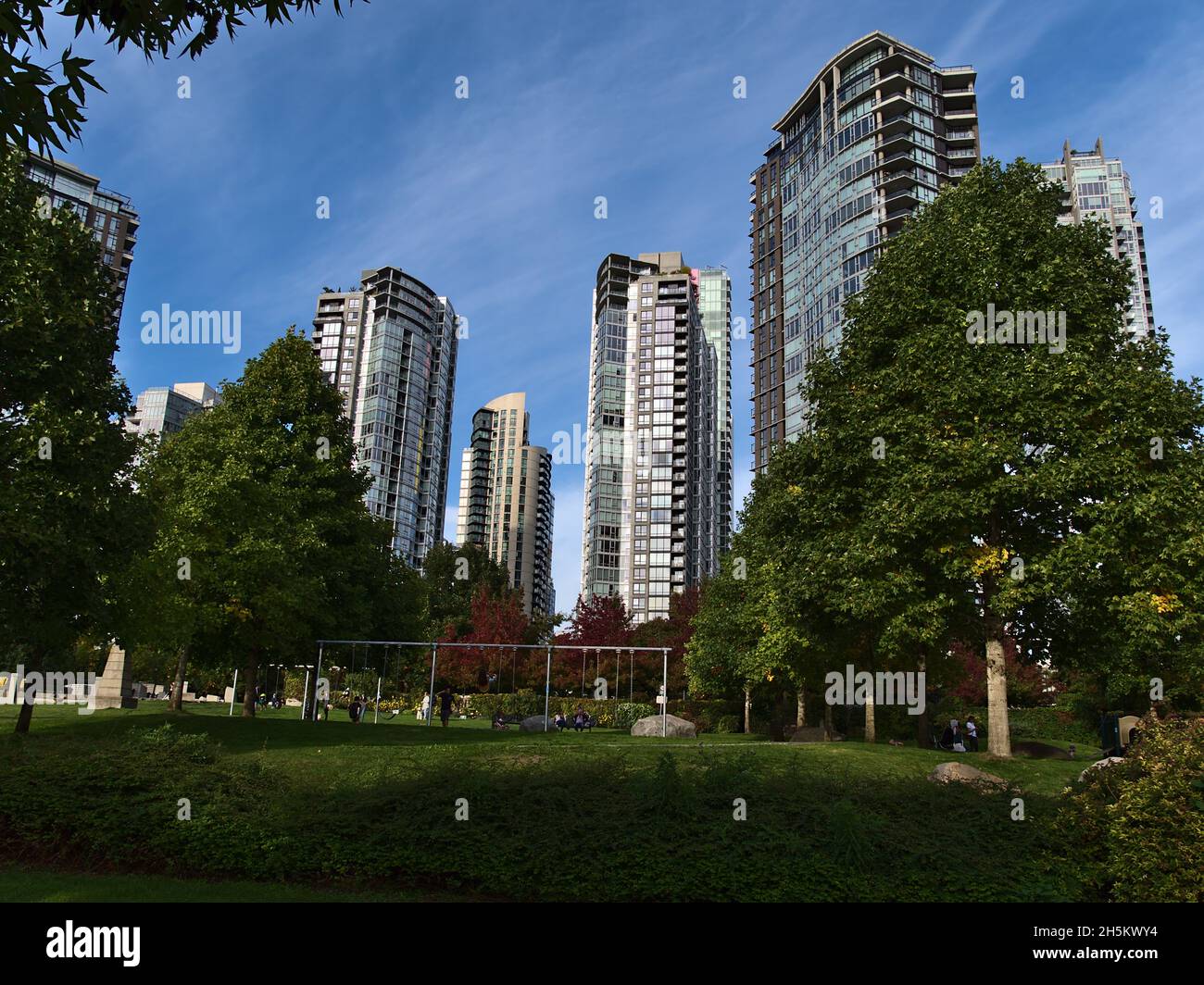 Menschen, die die Herbstsonne im George Wainborn Park am Ufer der False Creek Bay in der Innenstadt von Vancouver, British Columbia, Kanada mit Spielplatz genießen. Stockfoto