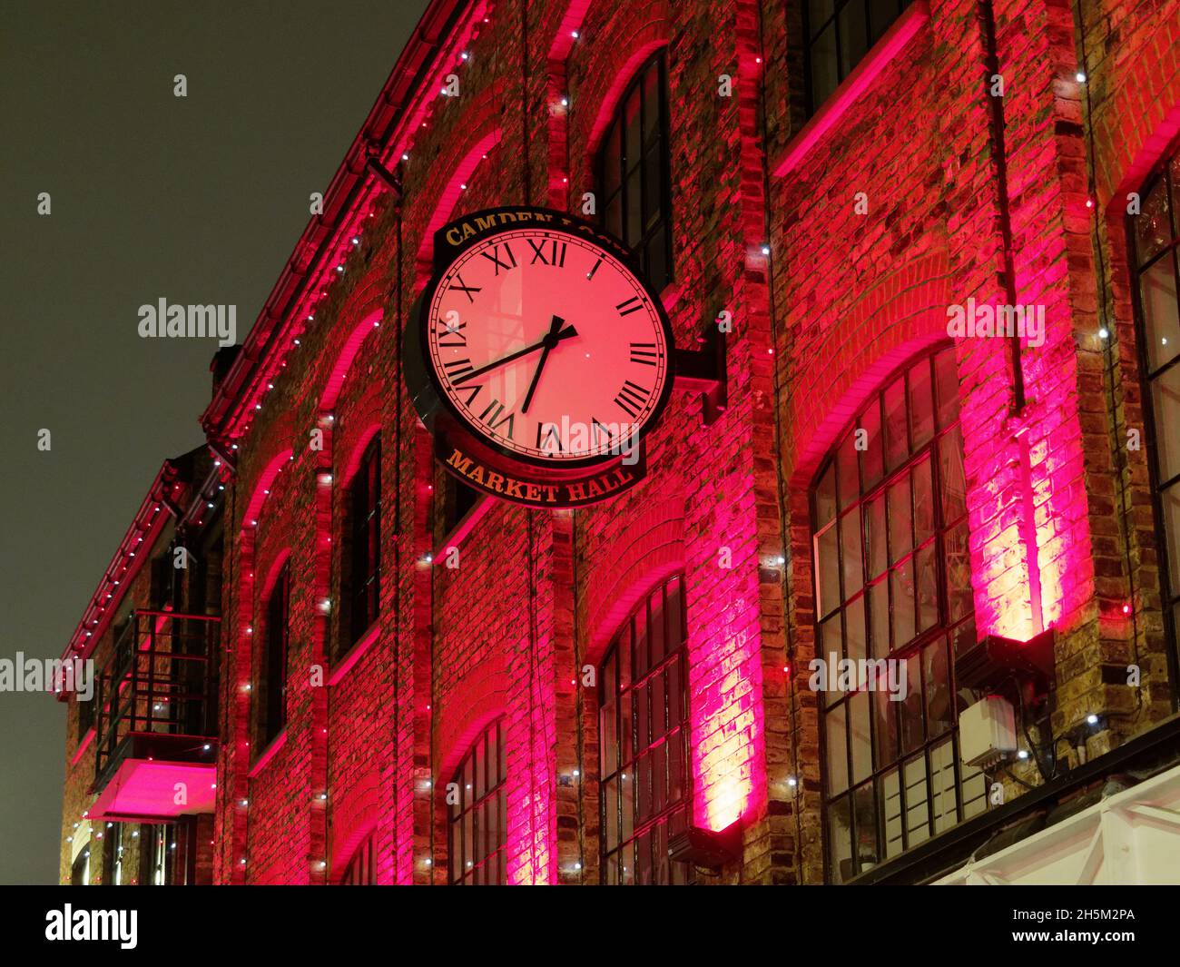 Farbenfroher Blick bei Nacht auf die Uhr an der Wand der Market Hall in Camden London Stockfoto