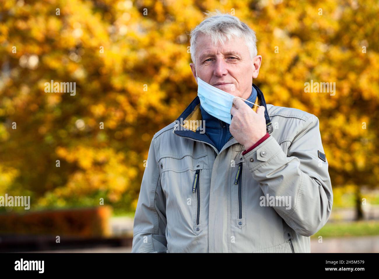 Älterer kaukasischer Mann mit blauer Gesichtsmaske im Gesicht, Herbstsaison Stockfoto