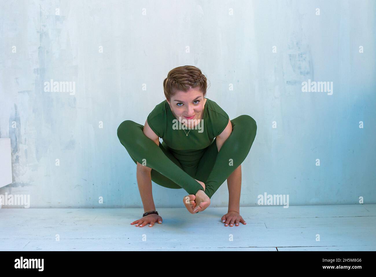 Ein Mädchen in grüner Sportkleidung führt einen Handstand, eine Pose im Yoga, in der Nähe einer hellen Wand durch Stockfoto