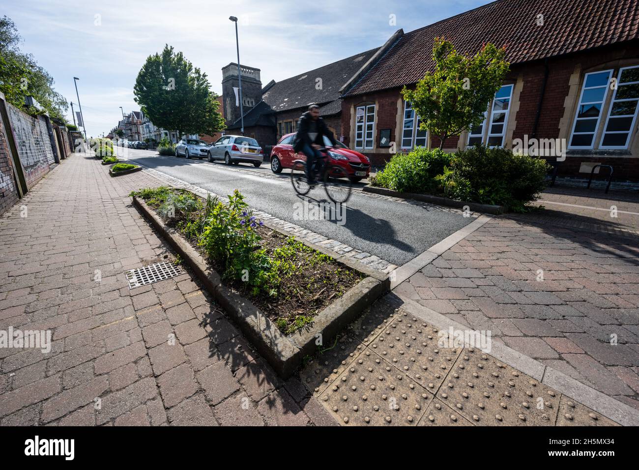 Ein Radfahrer fährt entlang einer verkehrsberuhigten Straße mit Quetschstellen, informellen Fußgängerüberwegen, Bäumen und Regengartenpflanzen in einer Heimatzone in der Nähe Stockfoto