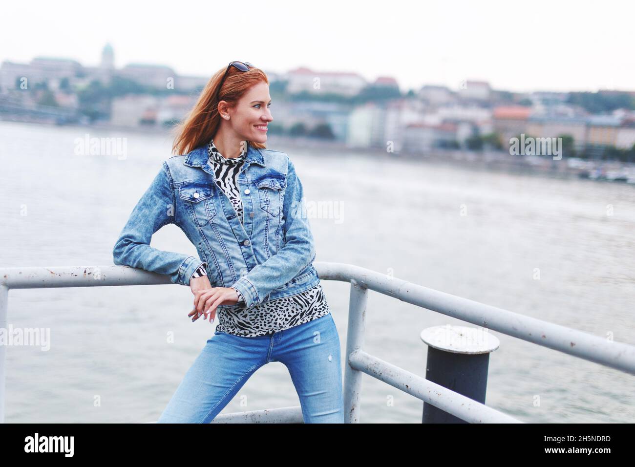 Junge rothaarige kaukasische modische Frau, die am Flussufer lächelt Stockfoto