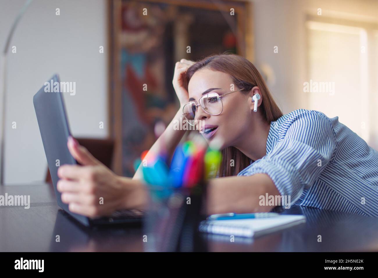 Junge Geschäftsfrau fragt sich über finanzielle Ergebnisse im Home Office, mit Laptop und Freisprecheinrichtung Stockfoto