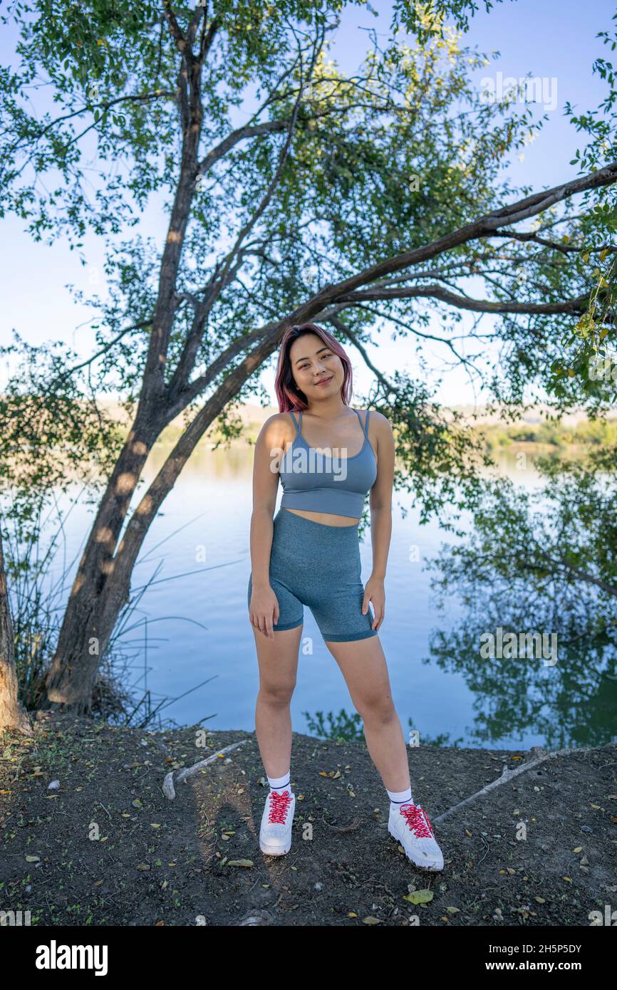 Junge asiatische Frau im strahlenden Sonnenlicht, die am Ufer eines idyllischen Sees sitzt Stockfoto
