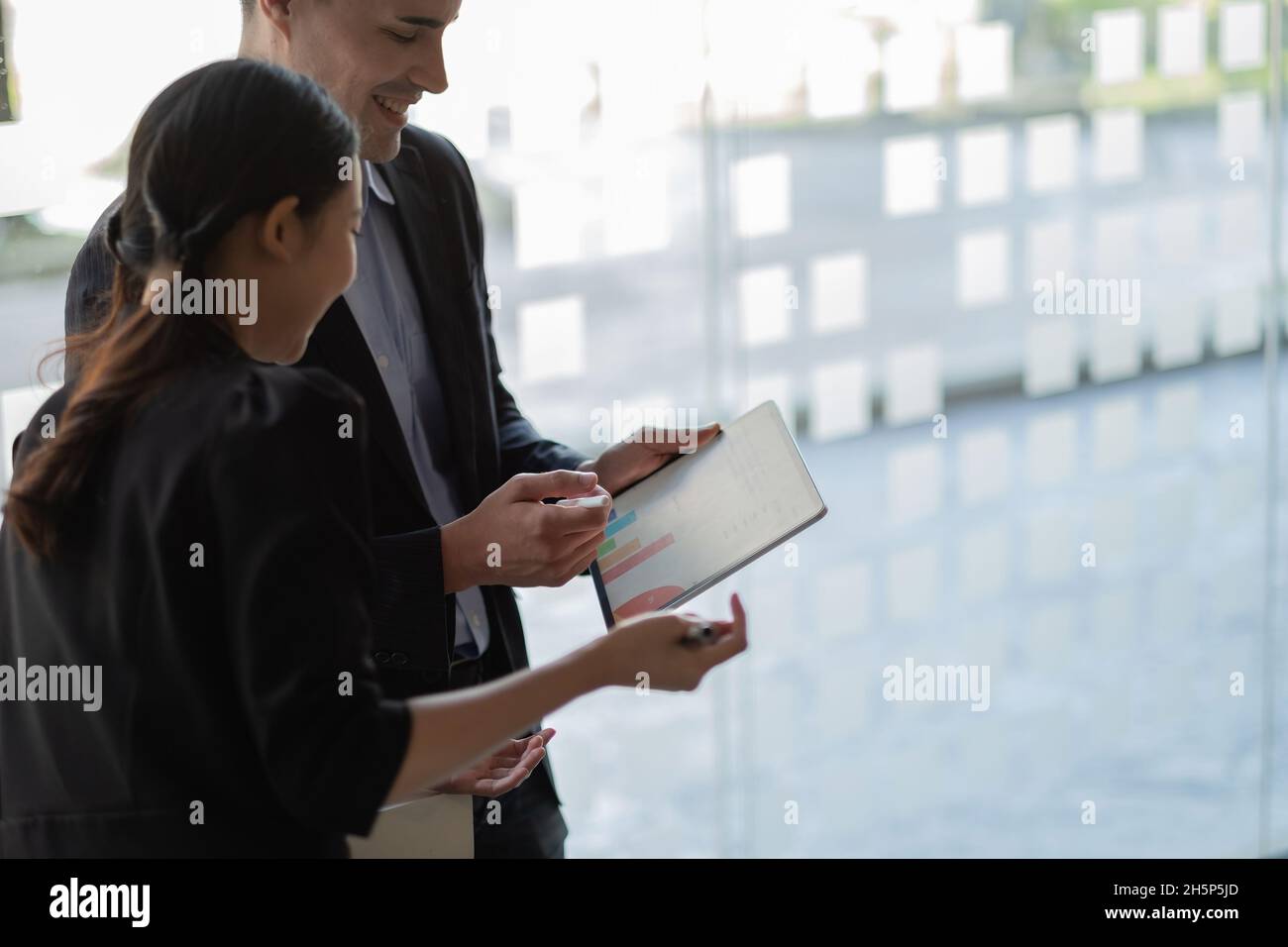Fokussierte Mitarbeiter verschiedener ethnischer Herkunft führen Brainstorming auf einem digitalen Tablet durch, asiatische und kaukasische Kollegen tauschen Ideen am Schreibtisch aus Stockfoto