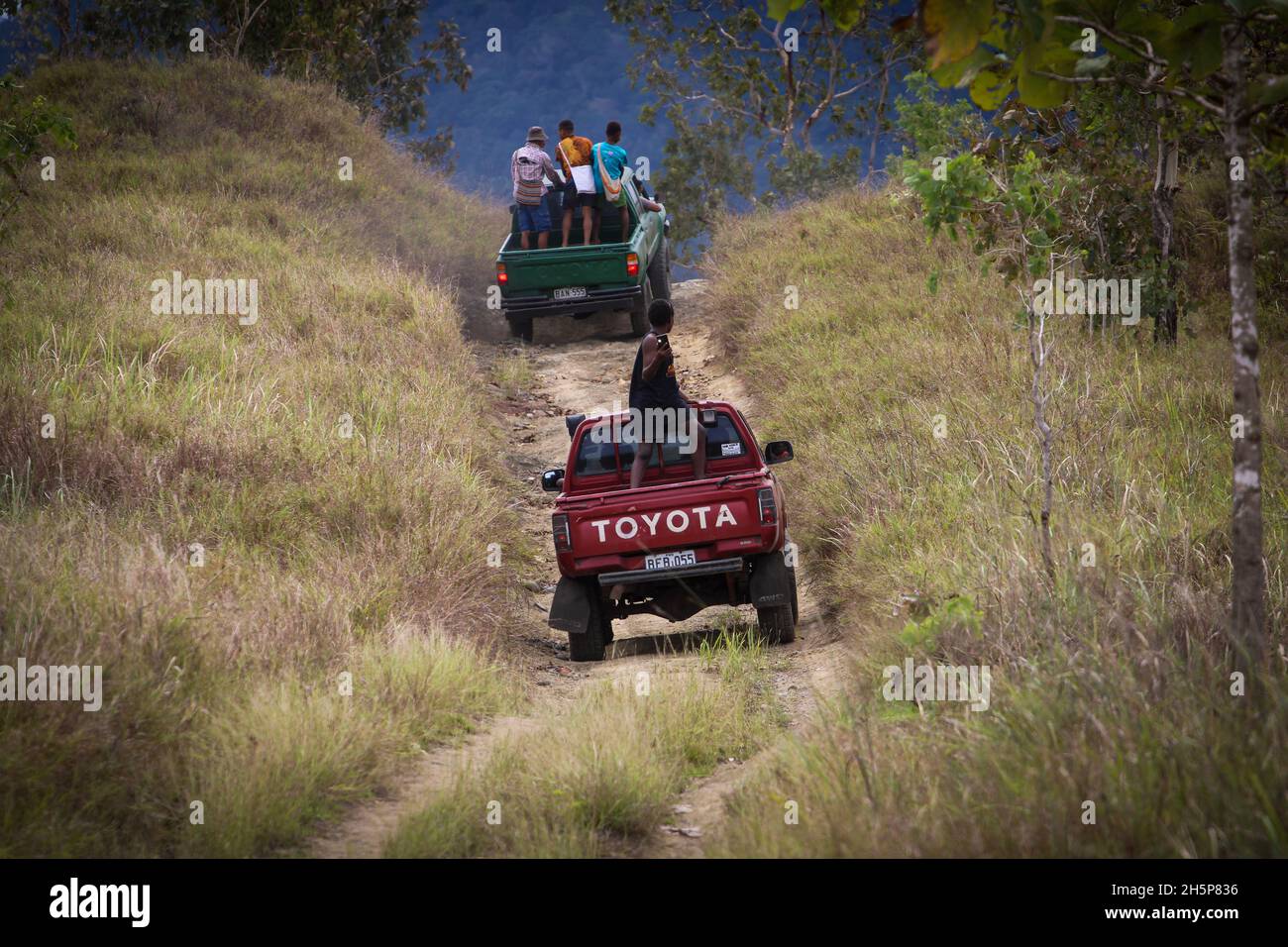 Ein paar alte Toyota Hilux Lastwagen, die auf einer Offroad-Strecke in der Zentralprovinz Papua-Neuguinea einen Hügel hochfahren Stockfoto