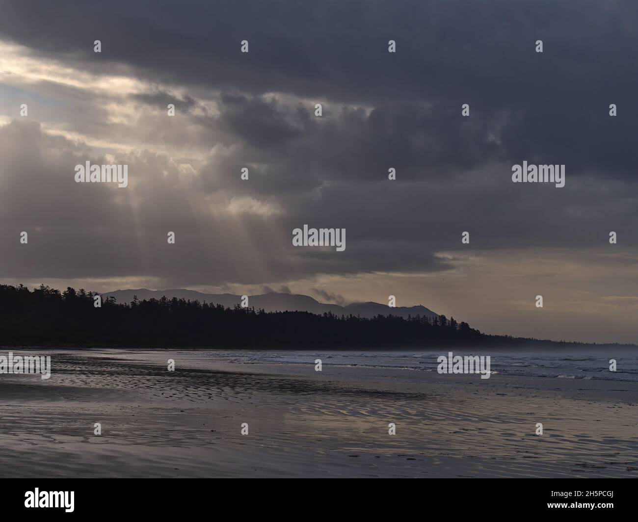Blick auf Long Beach am Morgen mit einem dramatischen Himmel aus Wolken und Sonnenstrahlen über der Silhouette des Regenwaldes im Pacific Rim National Park, Kanada. Stockfoto