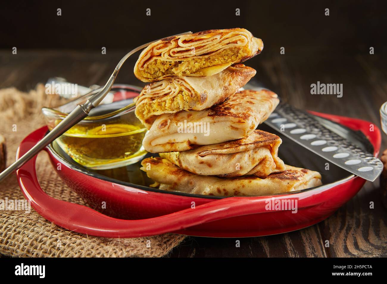 Pfannkuchen mit Fleisch, die auf dunklem Holzboden in einem Stapel mit Butter und Zange auf dem Teller liegen Stockfoto