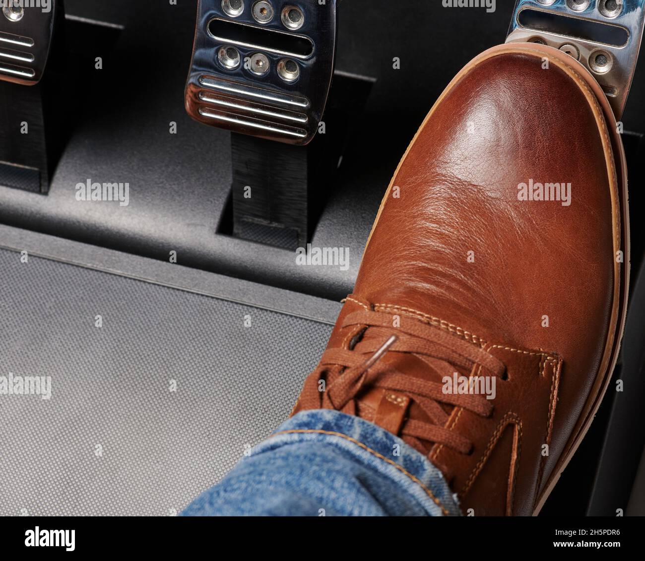 Thema „Beschleunigung im Auto“. Betätigen Sie das Gaspedal mit braunen Schuhen in glänzendem Metall Stockfoto