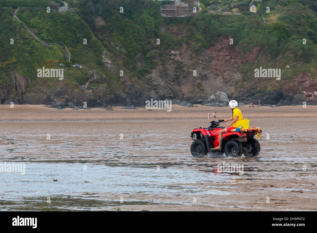 Ein RNLI-Rettungsschwimmer fährt ein Geländefahrzeug über Bantham Beach in Devon, Großbritannien Stockfoto