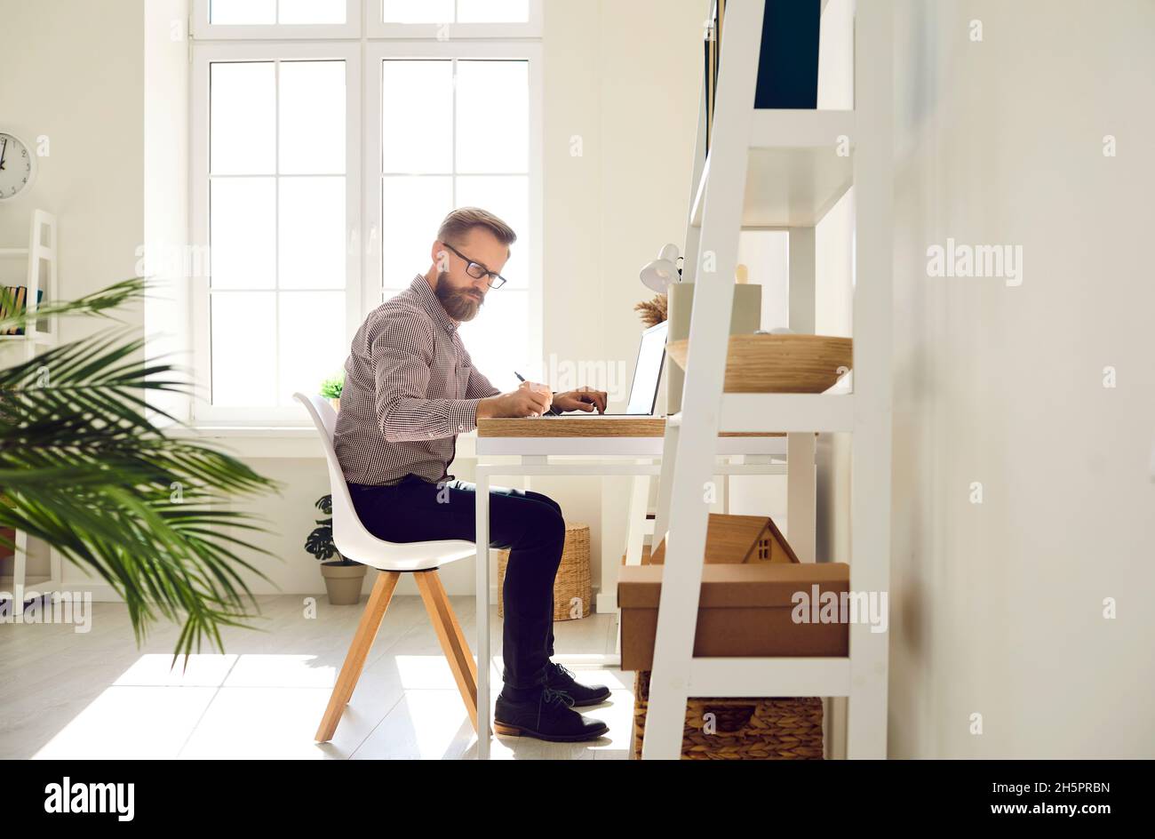 Seriös fokussierter Geschäftsmann, der an einem wichtigen Arbeitsprojekt in seinem hellen Home Office arbeitet. Stockfoto